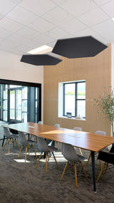 Two black hexagonal acoustic panels suspended from ceiling above conference table in office space.