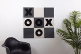 Wall-mounted tic-tac-toe game with black X and O symbols on alternating dark gray and cream squares.