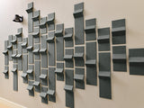 Gray three-dimensional wall tiles in varying sizes arranged in an abstract pattern on a beige wall.