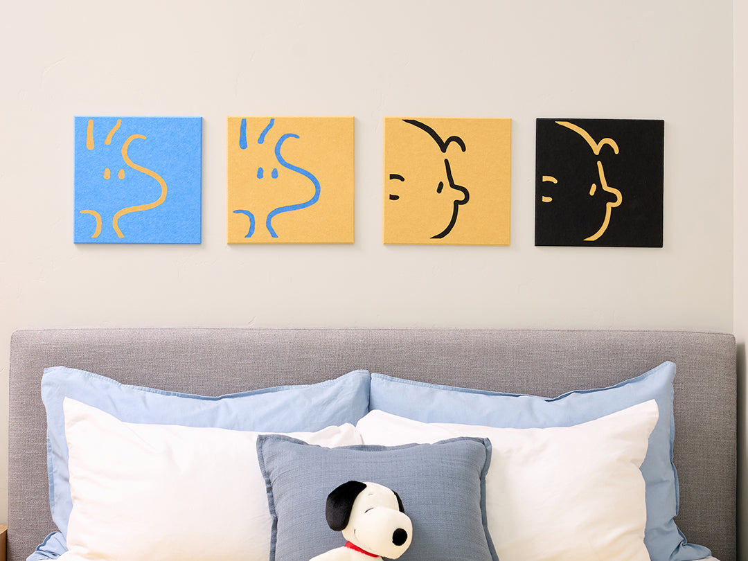 4 felt Charlie and Woodstock tiles on a wall above a bed with decorative pillows.