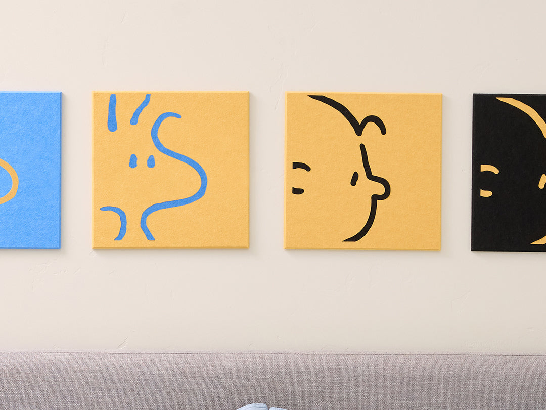 close up of 4 felt Charlie and Woodstock tiles on a wall above a bed with decorative pillows.