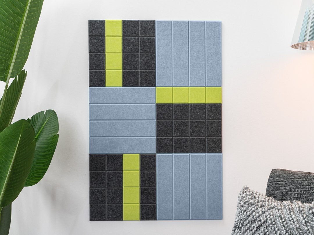 Felt Right wall art design on a white wall using blue, grey, and green felt tiles next to a house plant and a chair.