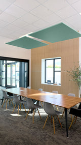 Two green square acoustic ceiling baffles suspended above a conference table in an office space.