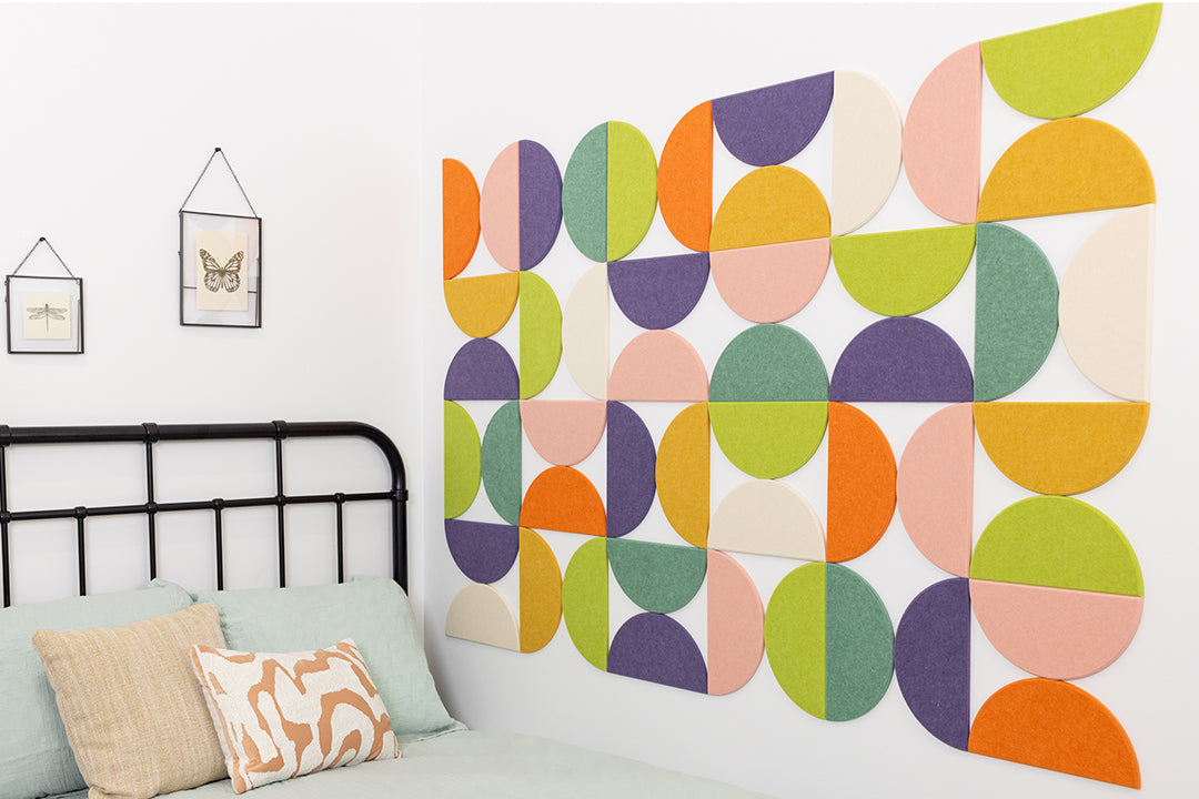 A Felt Right Wall Design using half circles in colorful geometric patterned wall decor above a bed in a room with two framed pictures and a pillow.