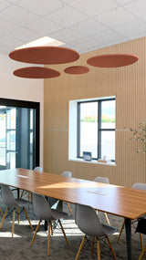 Four rust-colored oval acoustic baffles suspended from ceiling in modern office meeting room.
