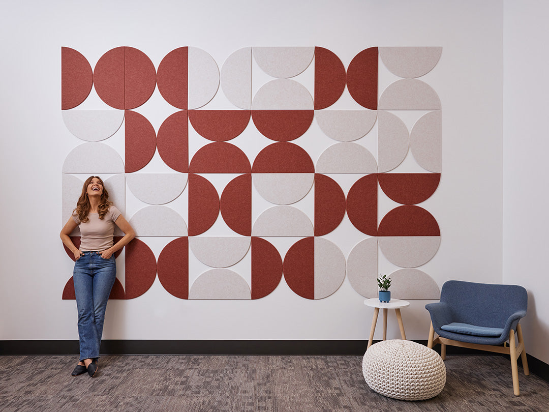 A Felt Right wall art design in shades of red and cream half circle tiles on a white wall with a chair and small side table.