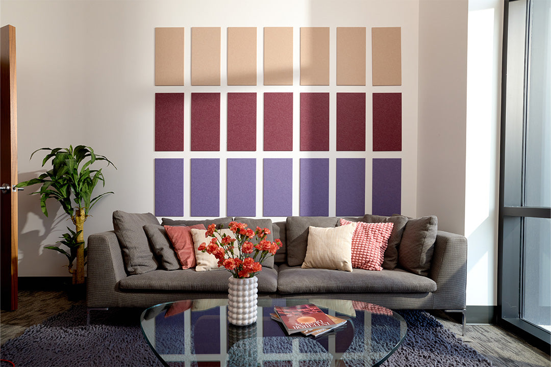 A Felt Right wall art design using rectangles to form a pattern in shades of purple and cream behind a couch and a plant.