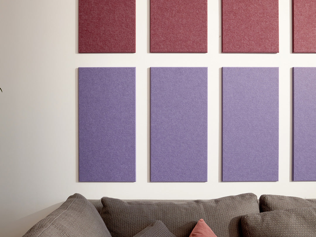 A Felt Right wall art design using rectangles to form a pattern in shades of purple and cream on a white wall above a couch.