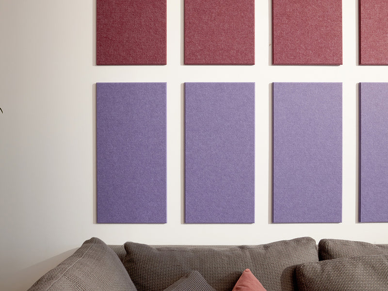 A Felt Right wall art design using rectangles to form a pattern in shades of purple and cream on a white wall above a couch.