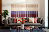 A Felt Right wall art design using rectangles in shades of creams and purples in an ombre pattern on a white wall above a couch in a room with a coffee table.