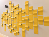 Yellow three-dimensional tiles arranged in a staggered wall pattern, creating depth and shadow variation against a beige back