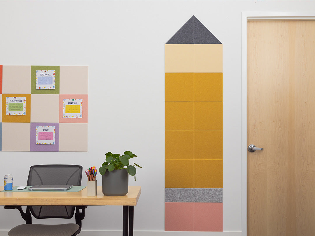 Room with a desk, plant, and wall decoration shaped like a pencil.
