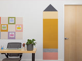 Room with a desk, plant, and wall decoration shaped like a pencil.