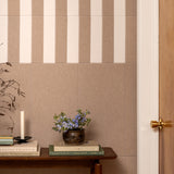 Wall with vertical striped pattern, table with books and plant, wooden door.