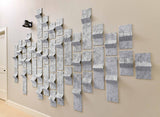 Wall art made of interlocking geometric shapes in various shades of gray on a beige wall.