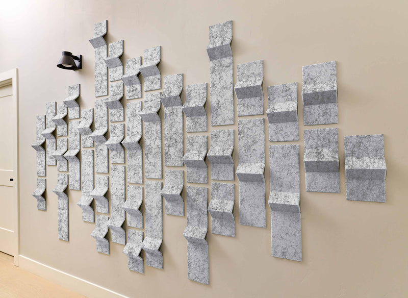 Wall art made of interlocking geometric shapes in various shades of gray on a beige wall.