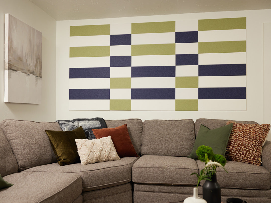 A Felt Right wall art design in shades of blue, green, and white on a white wall in a living room above a couch 