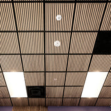 Wood slat ceiling panels arranged in a grid with black metal grid lines, recessed square lights, smoke detectors, and a ventilation opening.
