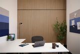 Modern office desk with laptop, plant, and decor against a wooden panel wall.