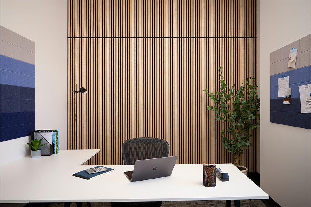 Modern office desk with laptop, plant, and decor against a wooden panel wall.