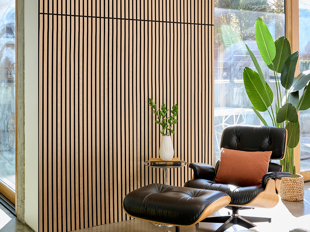 Modern black leather chair with a brown pillow in a room with large windows and plants.