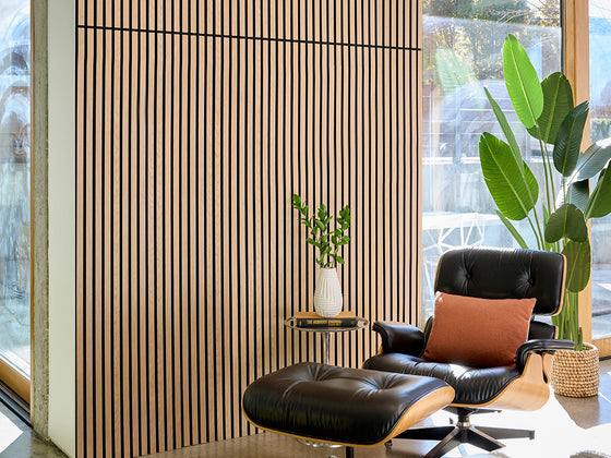 Modern black leather chair with a brown pillow in a room with large windows and plants.