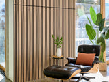 Black wood slat wall paneling sample displayed in interior setting with furniture and plants.