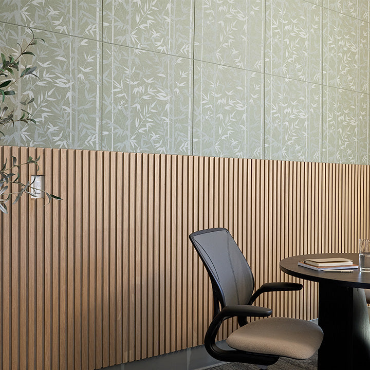 A modern interior corner with a light wood slatted wall paneling, a pale green patterned upper wall, a black office chair with a beige seat, and a dark round table holding books and a glass.