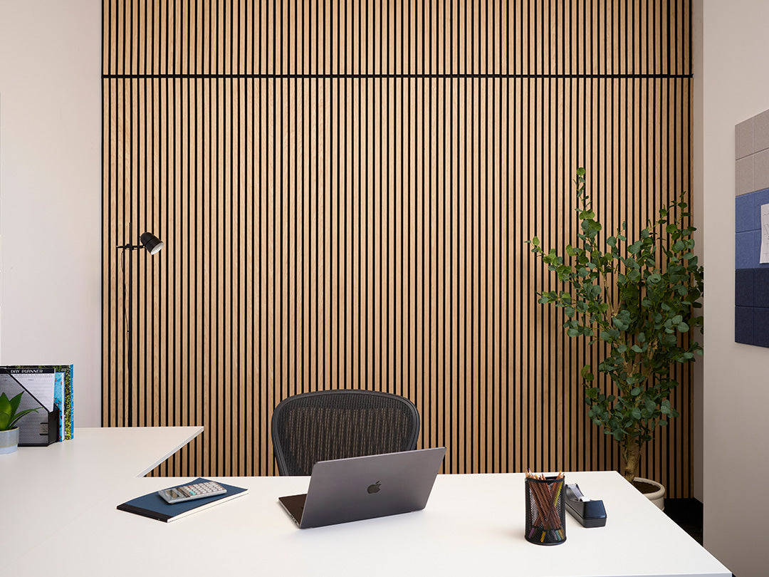 Modern office desk with laptop, plant, and chair against a wooden panel wall.