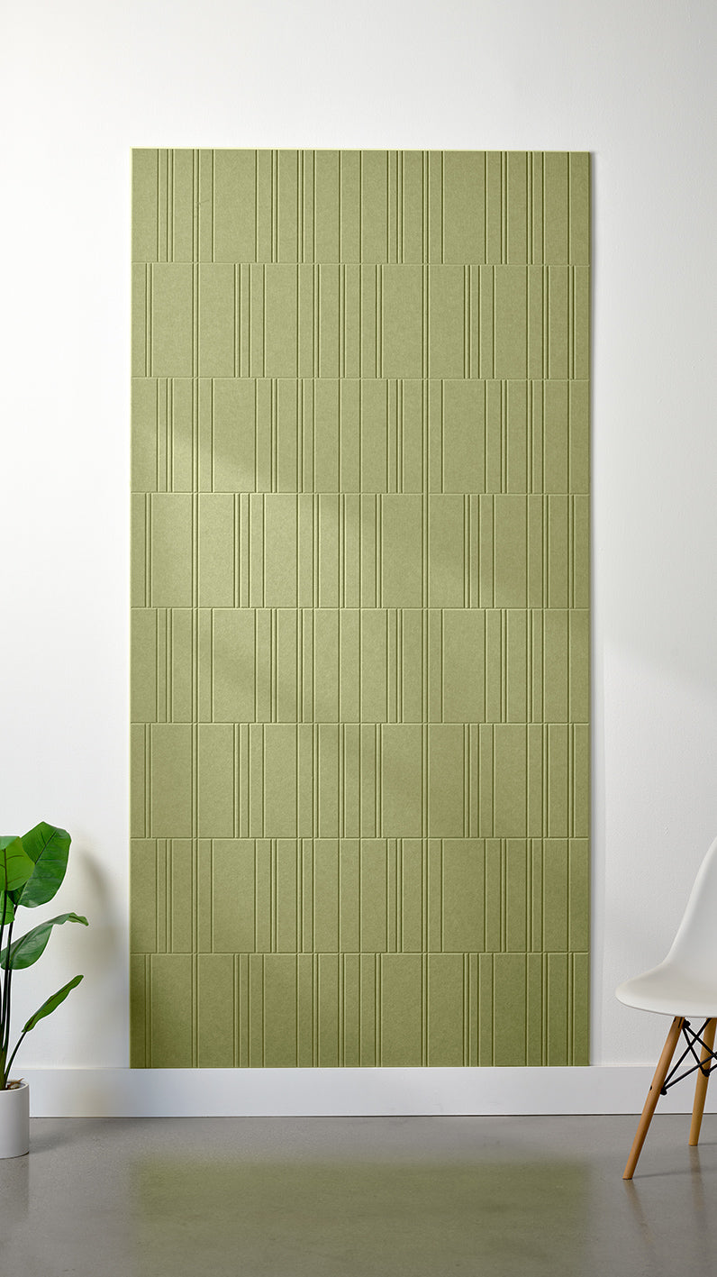 Aloe green Felt Right 4’ x 8’ PET felt panel with staggered lines engraved into the material against a white wall. A plant and chair are in the foreground.