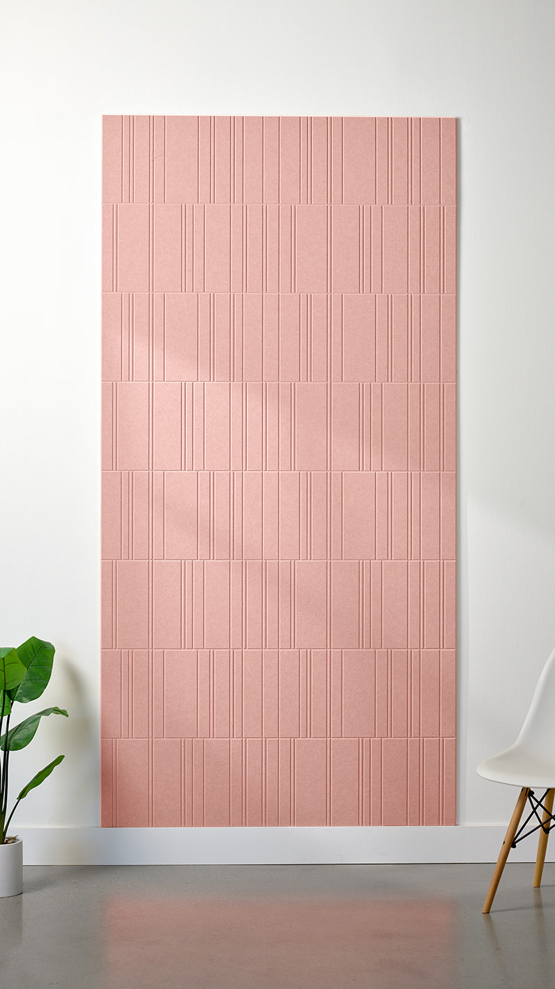 Light pink Felt Right 4’ x 8’ PET felt panel with staggered lines engraved into the material against a white wall. A plant and chair are in the foreground.