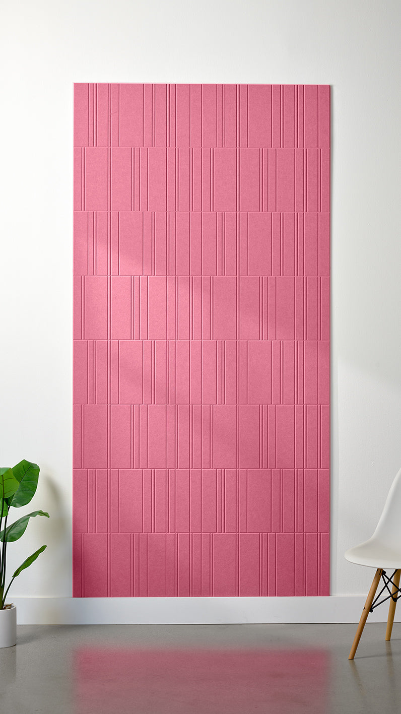 Hot pink Felt Right 4’ x 8’ PET felt panel with staggered lines engraved into the material against a white wall. A plant and chair are in the foreground.