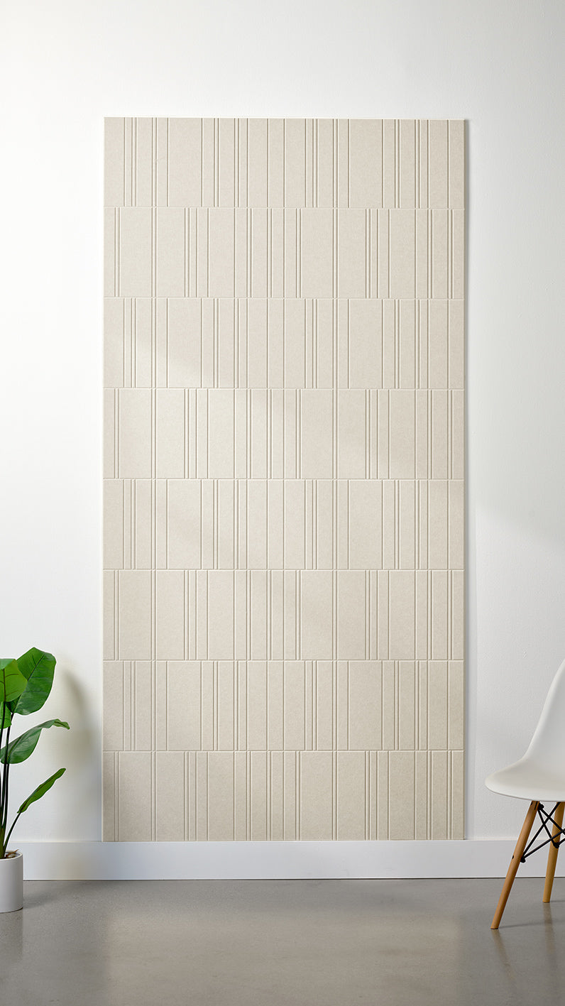 Ivory Felt Right 4’ x 8’ PET felt panel with staggered lines engraved into the material against a white wall. A plant and chair are in the foreground.