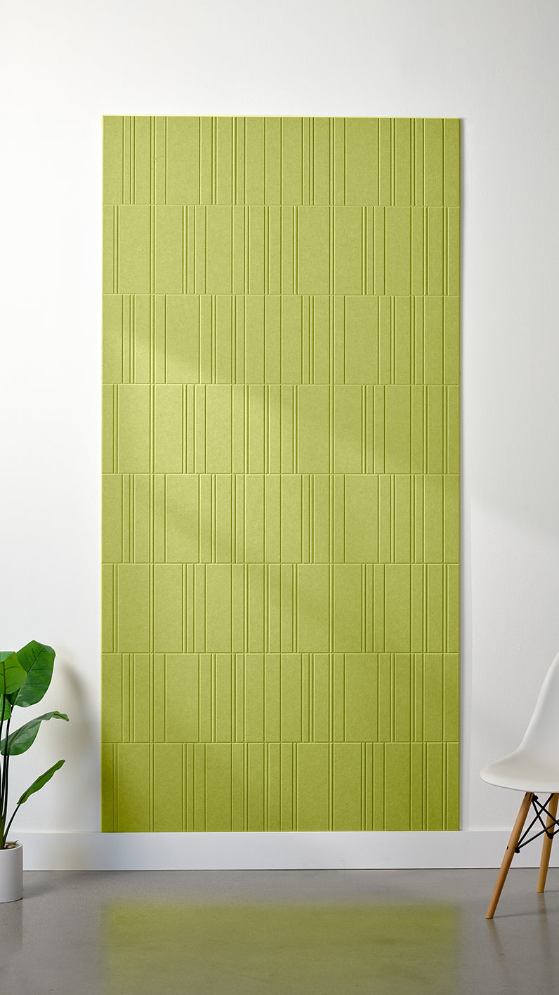 Bright green Felt Right 4’ x 8’ PET felt panel with staggered lines engraved into the material against a white wall. A plant and chair are in the foreground.