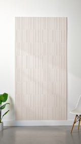 Heathered beige Felt Right 4’ x 8’ PET felt panel with staggered lines engraved into the material against a white wall. A plant and chair are in the foreground.
