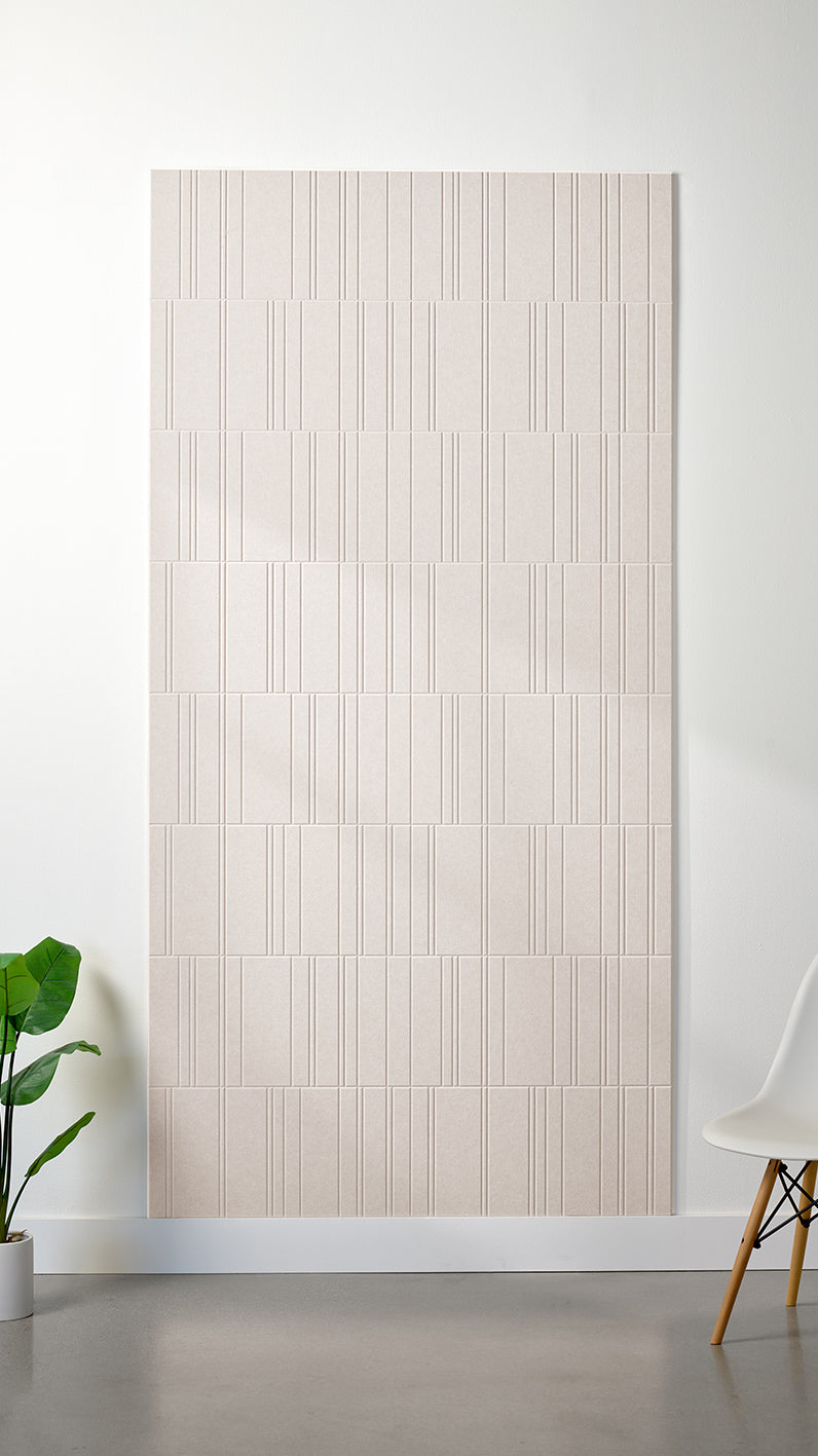 Heathered beige Felt Right 4’ x 8’ PET felt panel with staggered lines engraved into the material against a white wall. A plant and chair are in the foreground.