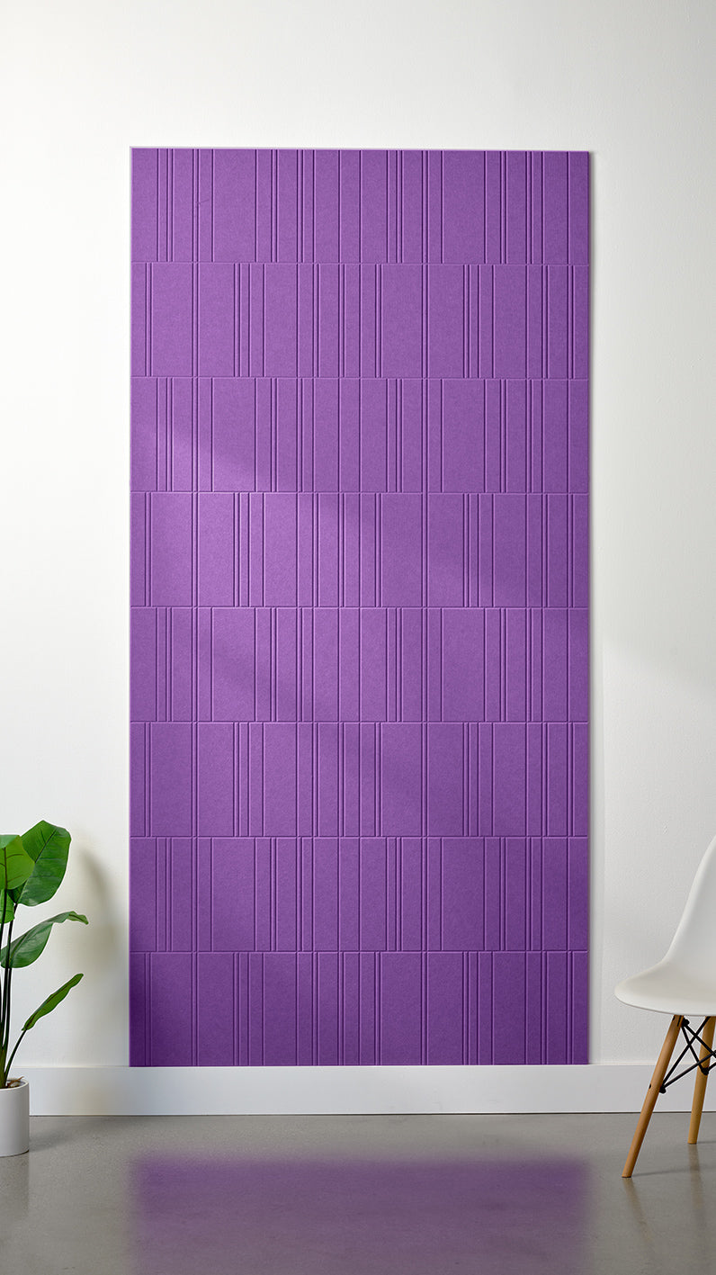 Lavender Felt Right 4’ x 8’ PET felt panel with staggered lines engraved into the material against a white wall. A plant and chair are in the foreground.