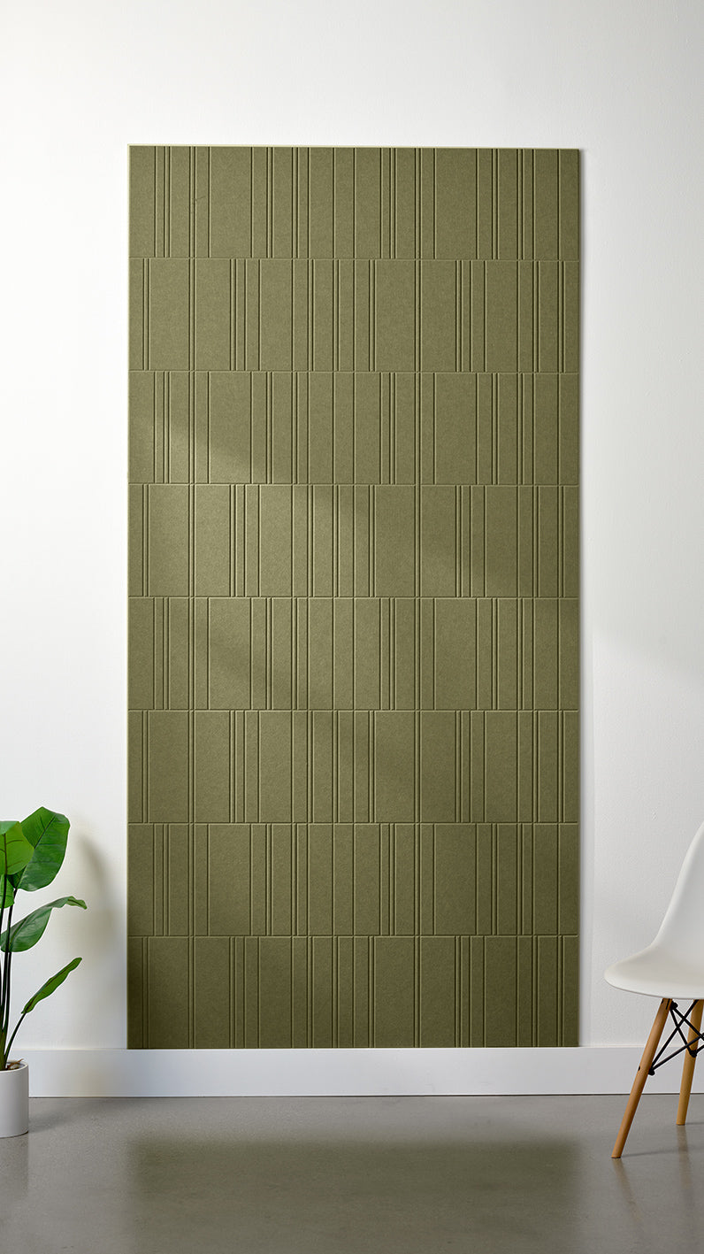 Olive green Felt Right 4’ x 8’ PET felt panel with staggered lines engraved into the material against a white wall. A plant and chair are in the foreground.