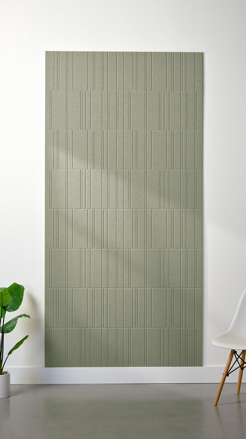 Sage green Felt Right 4’ x 8’ PET felt panel with staggered lines engraved into the material against a white wall. A plant and chair are in the foreground.