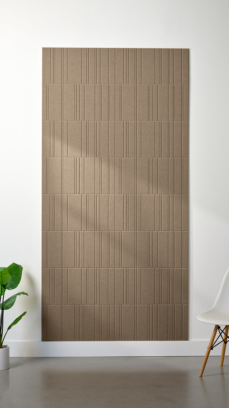 Light brown Felt Right 4’ x 8’ PET felt panel with staggered lines engraved into the material against a white wall. A plant and chair are in the foreground.