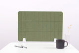 Sage green grid desk divider with white supports, positioned on white desktop with mug and pens.