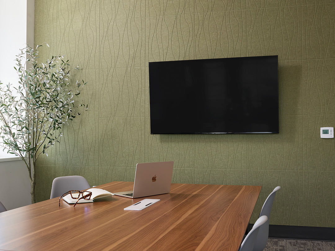 Conference room with a wooden table, laptop, and TV on a green wall.