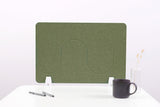 Green desk divider with wavy cutout design, white feet, positioned on white desk with mug and pens.