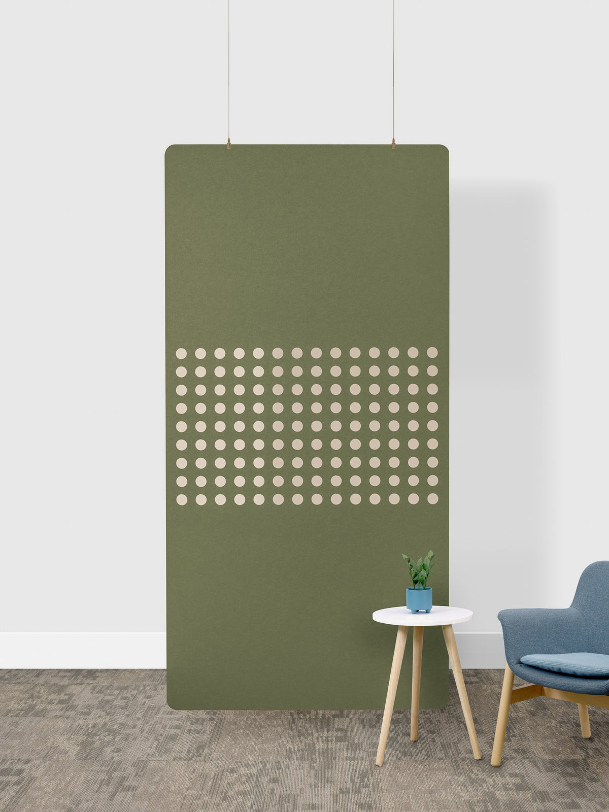 Green acoustic panel with circular cutouts on a white wall, with a small table and chair in the foreground.