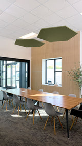 Two olive-green hexagonal acoustic panels suspended above a conference table in a modern office space.