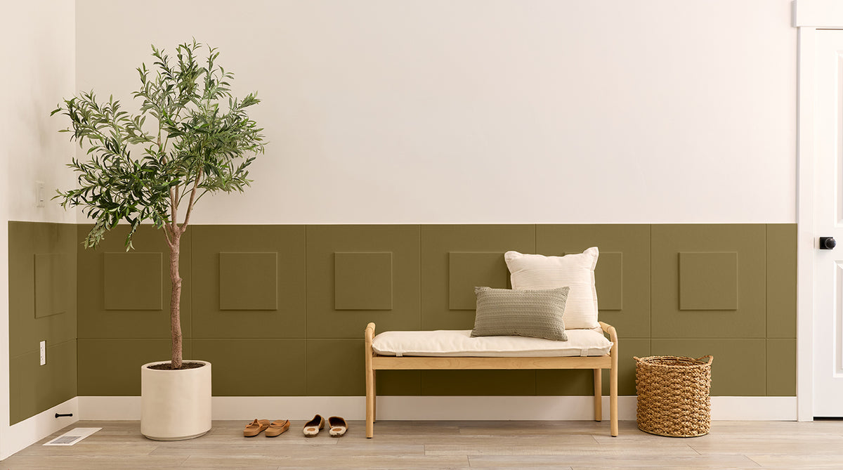 Entryway with a bench, plant, and shoes against a green paneled wall.