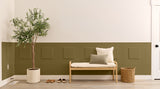 Entryway with a bench, plant, and shoes against a green paneled wall.