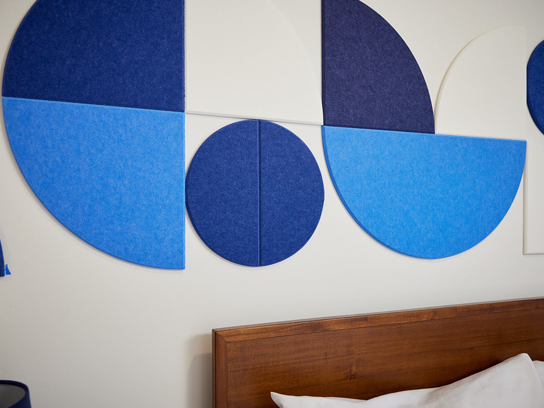Geometric blue wall art on a white wall with a wooden headboard.