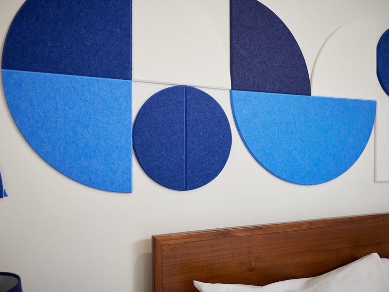 Geometric blue wall art on a white wall with a wooden headboard.