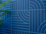 Blue geometric pattern with vertical stripes and curved lines, green plant visible on left side.